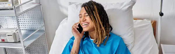 Jolly young african american woman talking by phone and smiling in her hospital ward, healthcare — Stock Photo