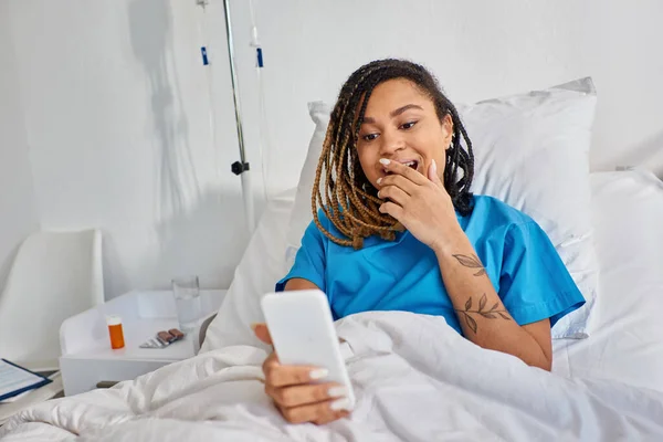 Atraente jovem afro-americana tendo vídeo chamada enquanto deitado na cama do hospital, cuidados de saúde — Fotografia de Stock