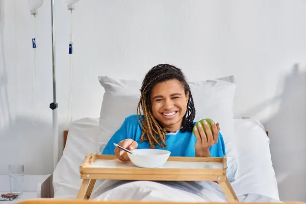 Giovane donna afroamericana con porridge e mela per colazione in reparto ospedaliero, assistenza sanitaria — Foto stock