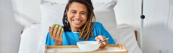 Jeune femme afro-américaine ayant du porridge et de la pomme pour le petit déjeuner en salle d'hôpital, soins de santé — Photo de stock