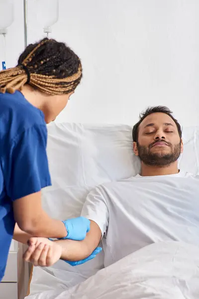 Enfermera afroamericana joven insertando catéter en el brazo de su paciente indio enfermo, cuidado de la salud - foto de stock