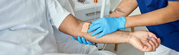 Cropped view of african american nurse inserting catheter into arm of her indian patient, banner — Stock Photo