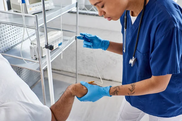 Обрізаний вид афроамериканської медсестри встановлює лічильник крапель для її індійського пацієнта, охорони здоров'я — стокове фото