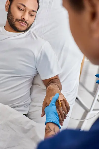 Vista recortada de enfermera afroamericana insertando catéter en el brazo de su paciente indio, cuidado de la salud - foto de stock