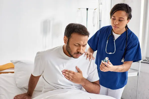 Young african american nurse giving asthma inhaler to her ill indian patient in his ward, healthcare — Stock Photo