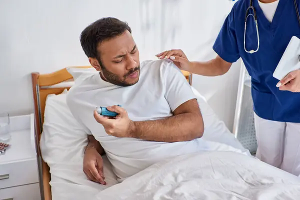 African american nurse helping her indian patient with asthma inhaler in his hospital ward — Stock Photo