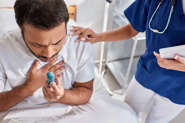 Африканская американская медсестра помогает своему индийскому пациенту с ингалятором от астмы в его больничном отделении — стоковое фото