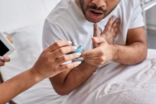 Vista recortada de la enfermera afroamericana dando inhalador al hombre indio que tiene problemas con la respiración - foto de stock