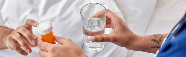 Vista ritagliata di infermiera afro-americana dando acqua e pillole al suo paziente indiano, banner — Foto stock