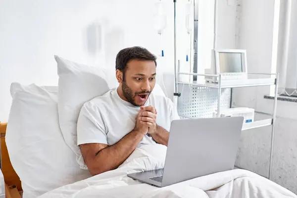 Surpreso alegre indiana paciente deitado na cama do hospital em sua ala olhando para o seu laptop, cuidados de saúde — Fotografia de Stock