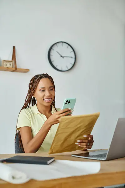 Joyeux beau vendeur afro-américain femme regardant son téléphone tout en tenant paquet post — Photo de stock
