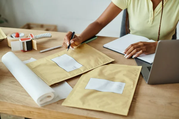 Обрезанный вид молодых африканских женщин-торговцев, подписывающих почтовые пакеты, концепция доставки — стоковое фото