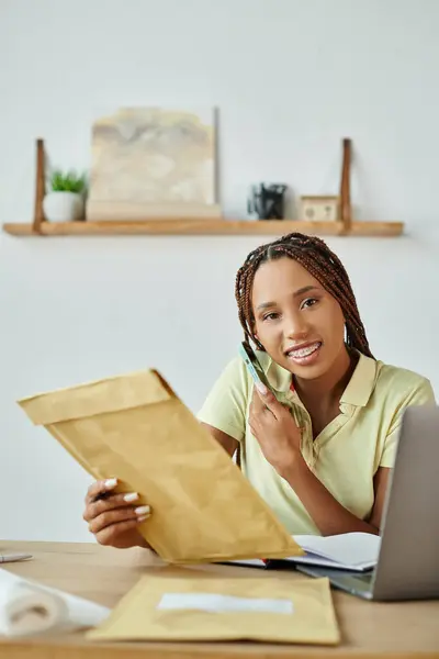 Attractive jolly african american seller talking by phone holding post packet and looking at camera — Stock Photo
