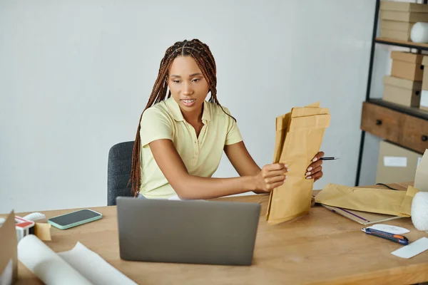 Fröhliche afrikanisch-amerikanische Verkäuferin mit Postpaketen und Blick auf Laptop, Lieferkonzept — Stockfoto