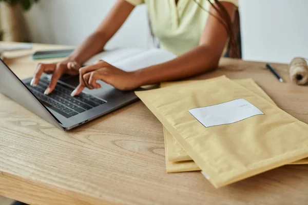 Vue recadrée de la jeune vendeuse afro-américaine tapant sur son ordinateur portable à côté des paquets de courrier — Photo de stock