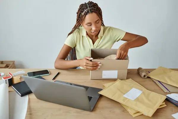 Good looking african american female retailer packing cardboard box attentively, delivery concept — Stock Photo