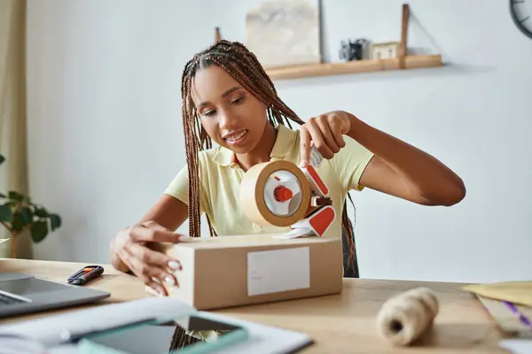Belle femme afro-américaine joyeux utilisant du ruban adhésif sur la boîte et souriant tout en travaillant, livraison — Photo de stock