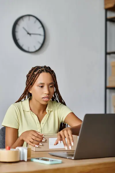 Gut aussehende afrikanisch-amerikanische Einzelhändlerin schaut auf ihren Laptop, während sie hart arbeitet, Lieferung — Stockfoto