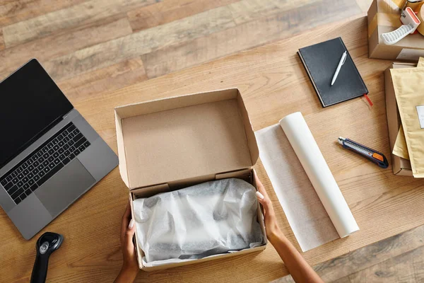 Cropped view of hard working african american woman packing box next to laptop, delivery concept — Stock Photo