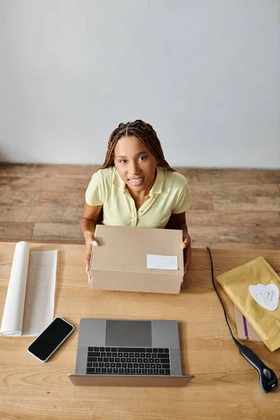 Joyeux jeune détaillant afro-américain femme tenant boîte et regardant la caméra, concept de livraison — Photo de stock