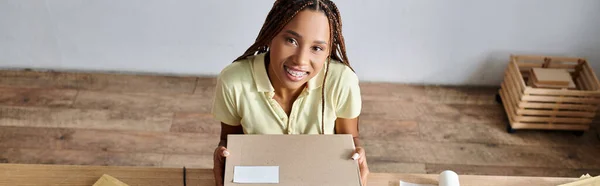 Cheerful pretty african american seller holding box and smiling at camera, delivery concept, banner — Stock Photo