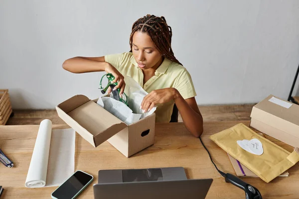Attrayant vendeur afro-américain femme emballage chaussures vertes dans la boîte pendant le travail, la livraison — Photo de stock