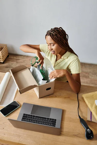 Joyeux jeune afro-américain femme détaillant emballage chaussures vertes dans la boîte, concept de livraison — Photo de stock