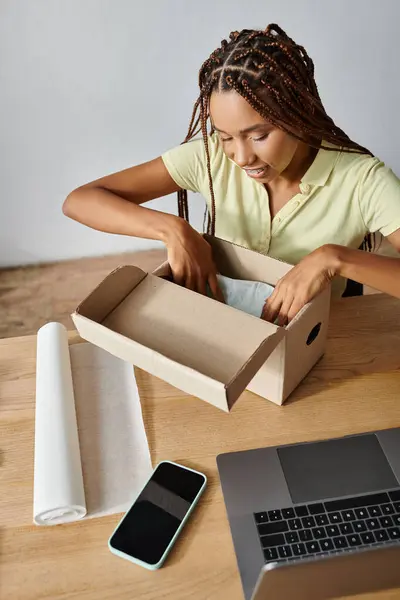 Alegre jovem afro-americana caixa de embalagem e sorrindo alegremente enquanto trabalhava duro, entrega — Fotografia de Stock