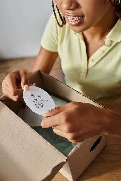 Vista cortada de jovem africano americano vendedor feminino colocando obrigado adesivo no pacote, entrega — Fotografia de Stock