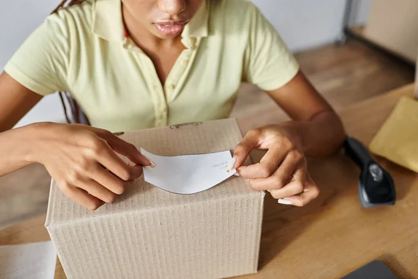 Vista cortada de trabalho duro Africano americano vendedor feminino colocando adesivo na caixa de papelão — Fotografia de Stock