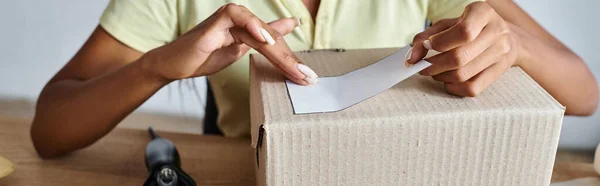 Cropped view of ambitious african american female retailer putting sticker on box, delivery, banner — Stock Photo
