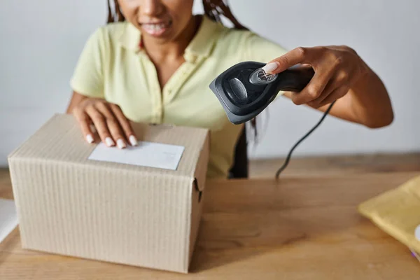 Cropped view with focus on cardboard box with blurred african american female seller scanning it — Stock Photo