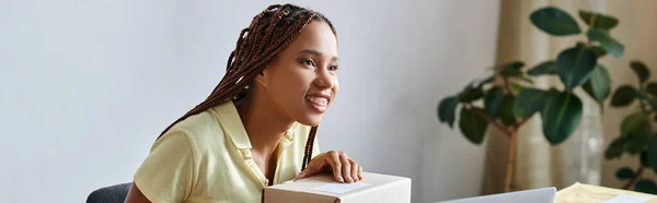Mujer afroamericana alegre sosteniendo el escáner al lado de la caja durante el trabajo, concepto de entrega, bandera - foto de stock