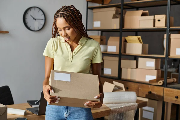 Attractive jolly african american female merchant holding cardboard box and smiling joyfully — Stock Photo
