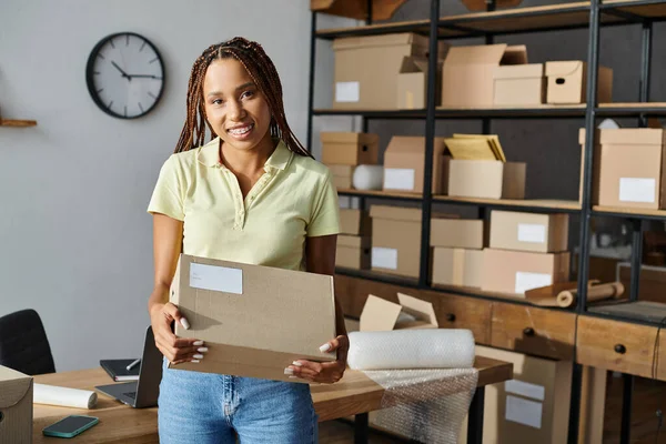 Appealing hard working african american female seller holding box and smiling at camera, delivery — Stock Photo
