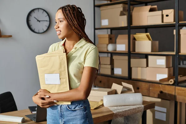 Belle femme afro-américaine avec bretelles tenant des paquets de courrier et détournant les yeux, concept de livraison — Photo de stock