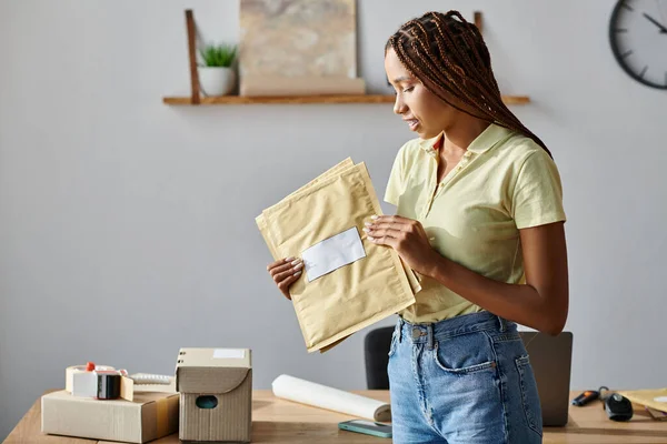 Привлекательная молодая африканская продавщица смотрит на почтовые пакеты во время работы, концепция доставки — стоковое фото