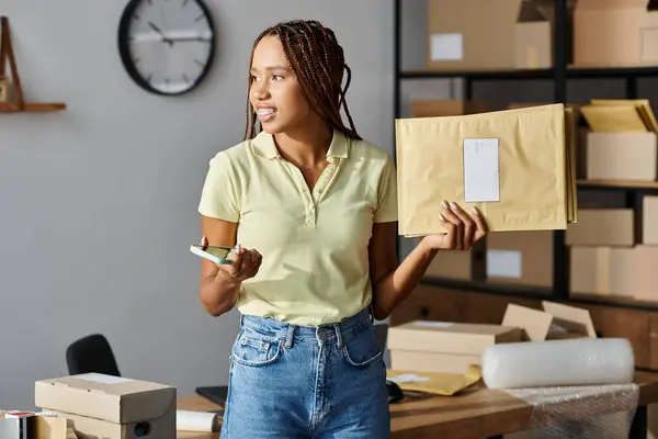 Atraente alegre Africano americano vendedor feminino segurando pacotes post e telefone e olhando para longe — Fotografia de Stock
