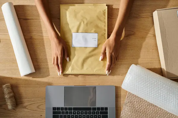 Cropped view of young african american female merchant holding post packets next to laptop, delivery — Stock Photo