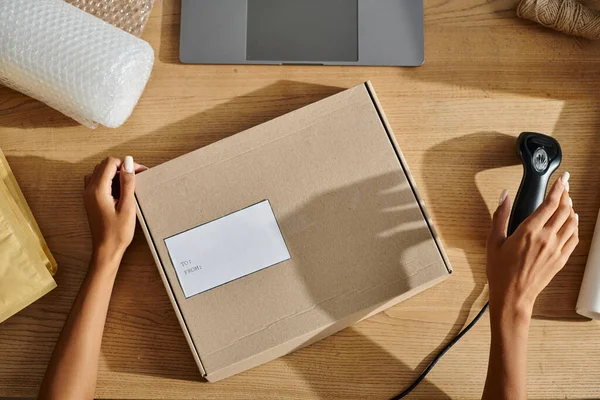Cropped view of african american female seller holding scanner next to cardboard box, delivery — Stock Photo
