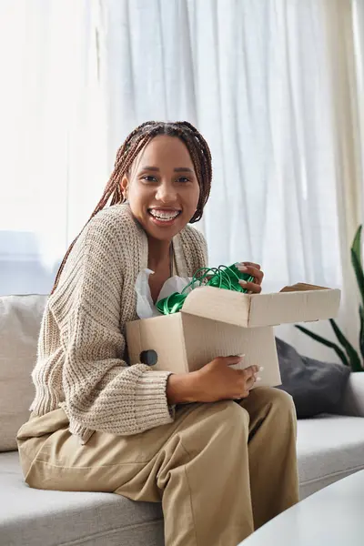 Graziosa donna americana africana allegra con bretelle che tengono la scatola con scarpe verdi e sorridente alla macchina fotografica — Foto stock