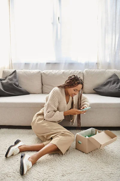 Jolly beautiful african american woman with braces taking photo of her parcel while sitting on floor — Stock Photo