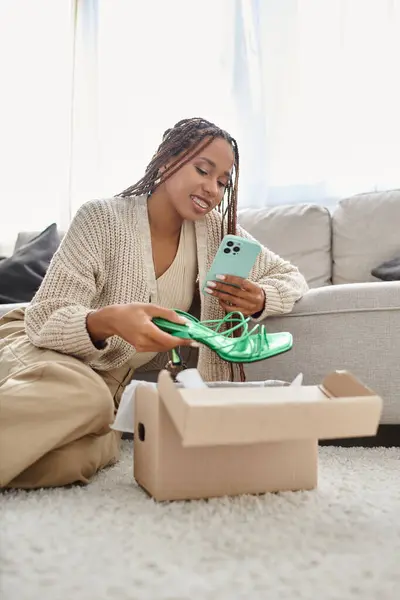 Belle femme afro-américaine joyeuse assise sur le sol et prenant des photos de nouvelles chaussures vertes — Photo de stock