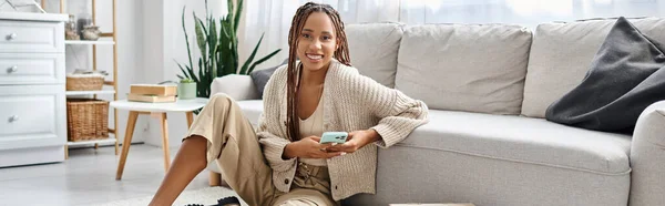 Jolie belle femme afro-américaine avec bretelles tenant le téléphone et souriant à la caméra, bannière — Photo de stock