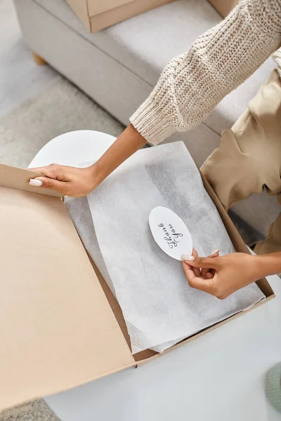 Cropped view of african american woman in homewear opening her parcel with thank you sticker on it — Stock Photo