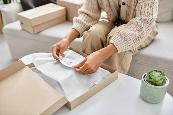 Cropped view of young african american woman in homewear unpacking parcel with thank you sticker — Stock Photo