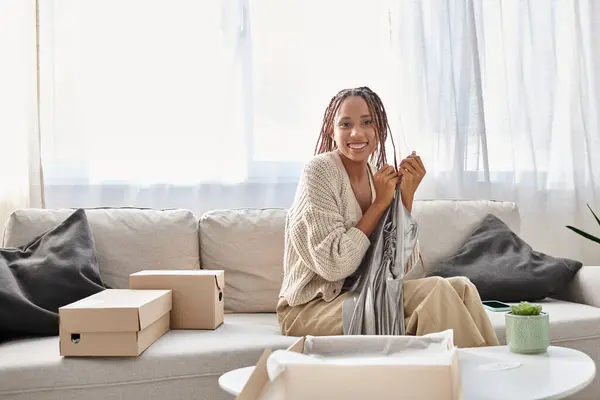 Joyful young african american woman holding her new silver dress she unpacked and smiling at camera — Stock Photo