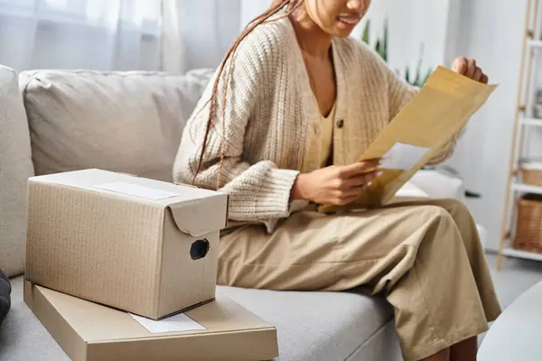Cropped view with focus on cardboard boxes next to blurred african american woman with post packet — Stock Photo