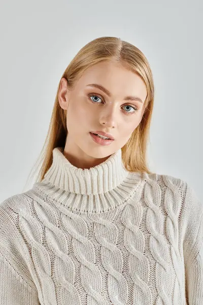 Portrait of beautiful blonde woman in  white knitted sweater looking at camera on grey, winter style — Stock Photo