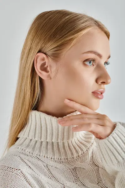 Портрет блондинки с натуральным макияжем в теплом свитере с рукой возле подбородка, зимняя красота — стоковое фото